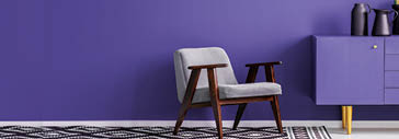 Grey armchair on patterned carpet next to violet cabinet with black vase in living room interior with copy space