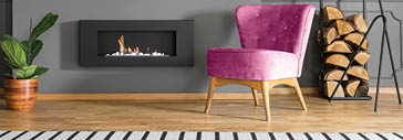 Green armchair and firewood next to fireplace in grey living room interior with lamp  Real photo
