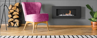 Green armchair and firewood next to fireplace in grey living room interior with lamp  Real photo